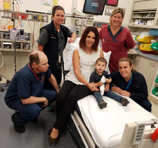 Hospital room with a child (Levi) on the bed being held by mother (Cindy) while four of the hosputal's staff look on