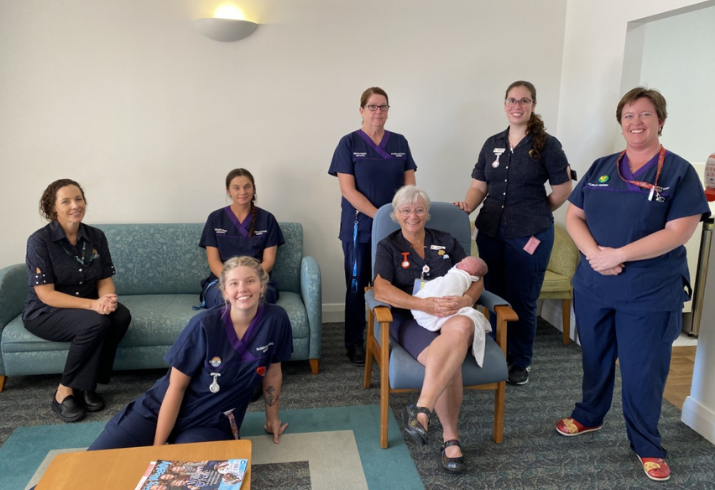 A group shot of midwives physically distanced, some standing, some seated and one holding a newborn baby.