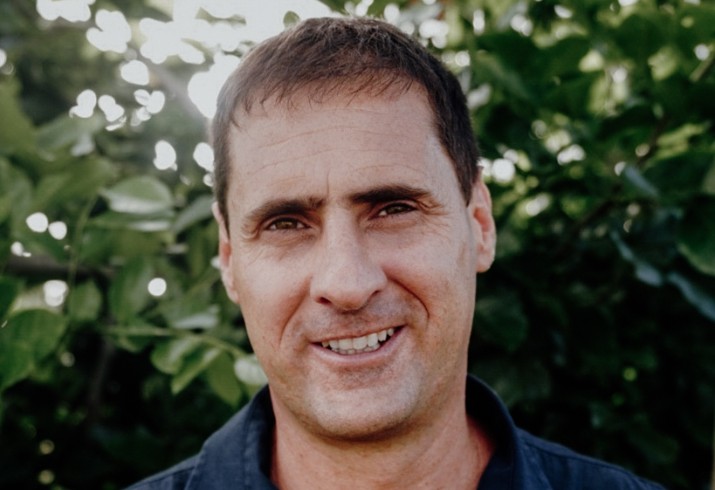 Dr Yehuda Levy stands in front of leafy green background 