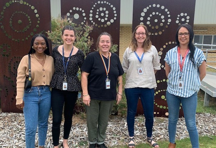 Five peer support workers standing in front of Aboriginal artwork outside health service