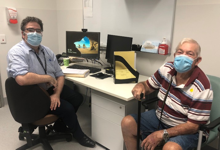 Doctor and patient sit at desk with masks on for consultation