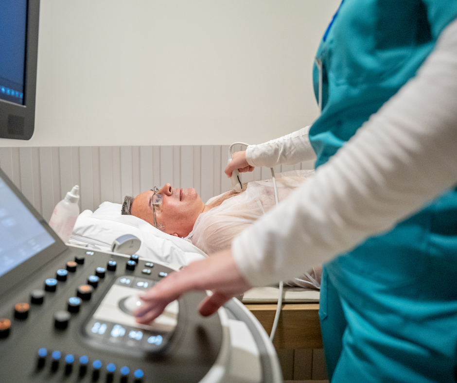 A patient lays flat on a bed while a sonographer checks his heart using a songraphy wand attached to a computer screen.