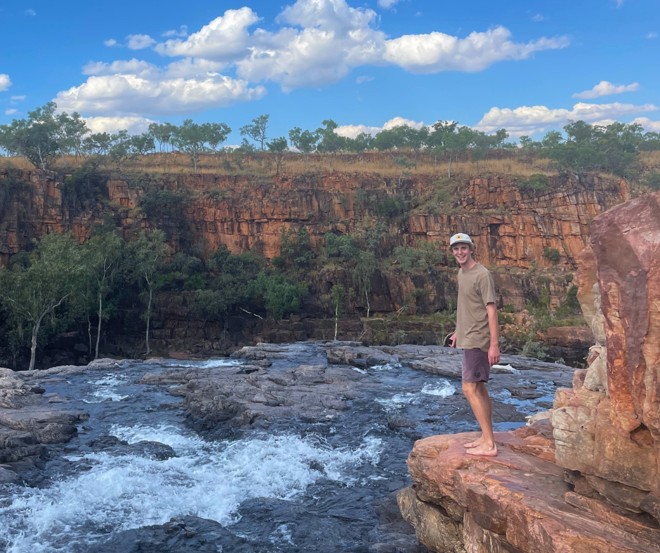 A young man stands by a waterfall smiling