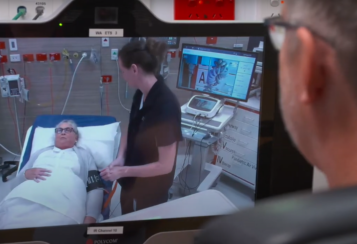 A clinician views a patient and nurse in a hospital room via a screen.