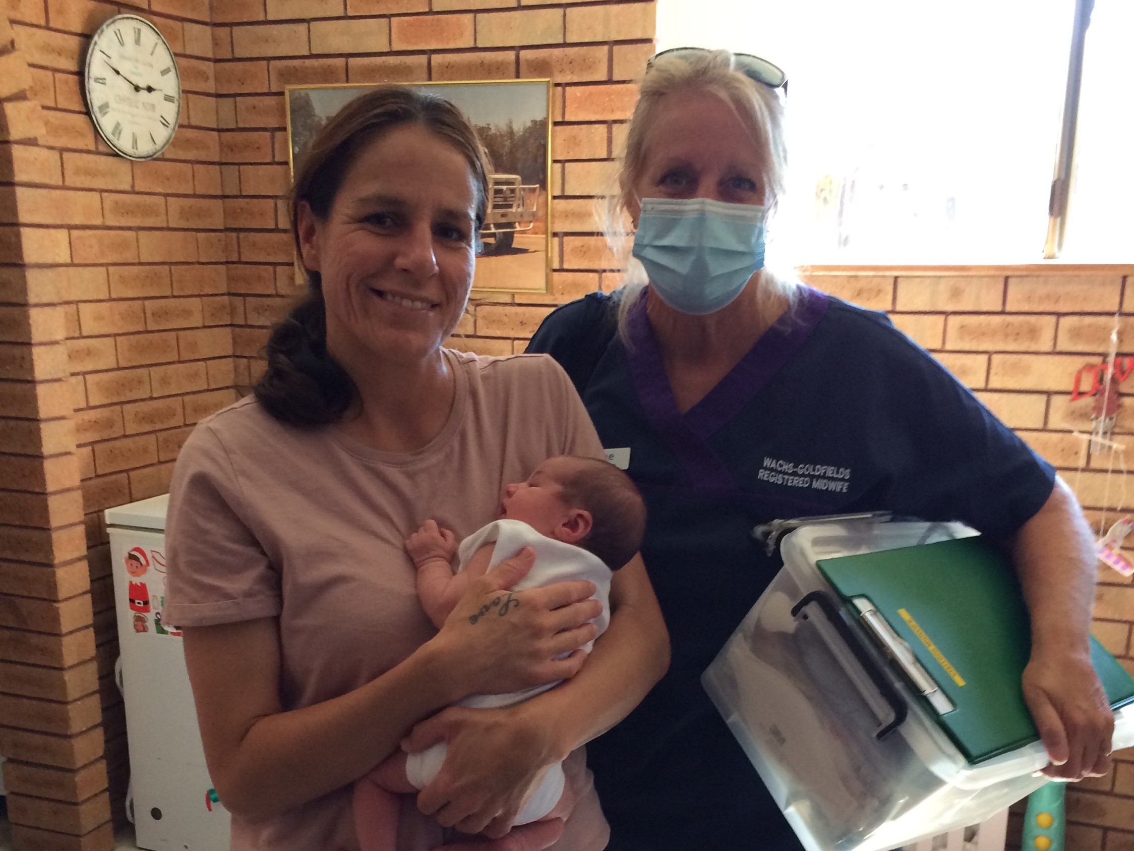 A mother holds a small baby while a masked nurse looks on