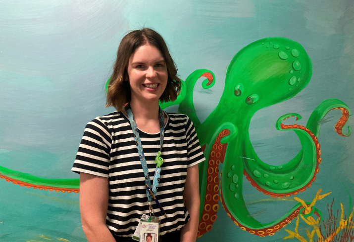 A young woman stands in front of a mural painted wall featuring an octopus cartoon 