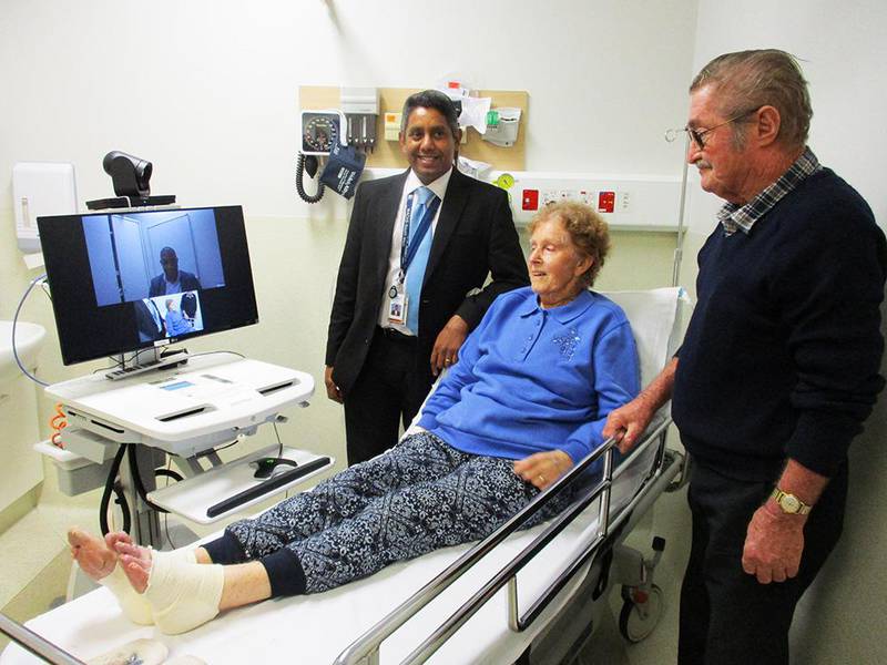 A patient speaks to a stroke specialist via telehealth while her doctor and husband look on