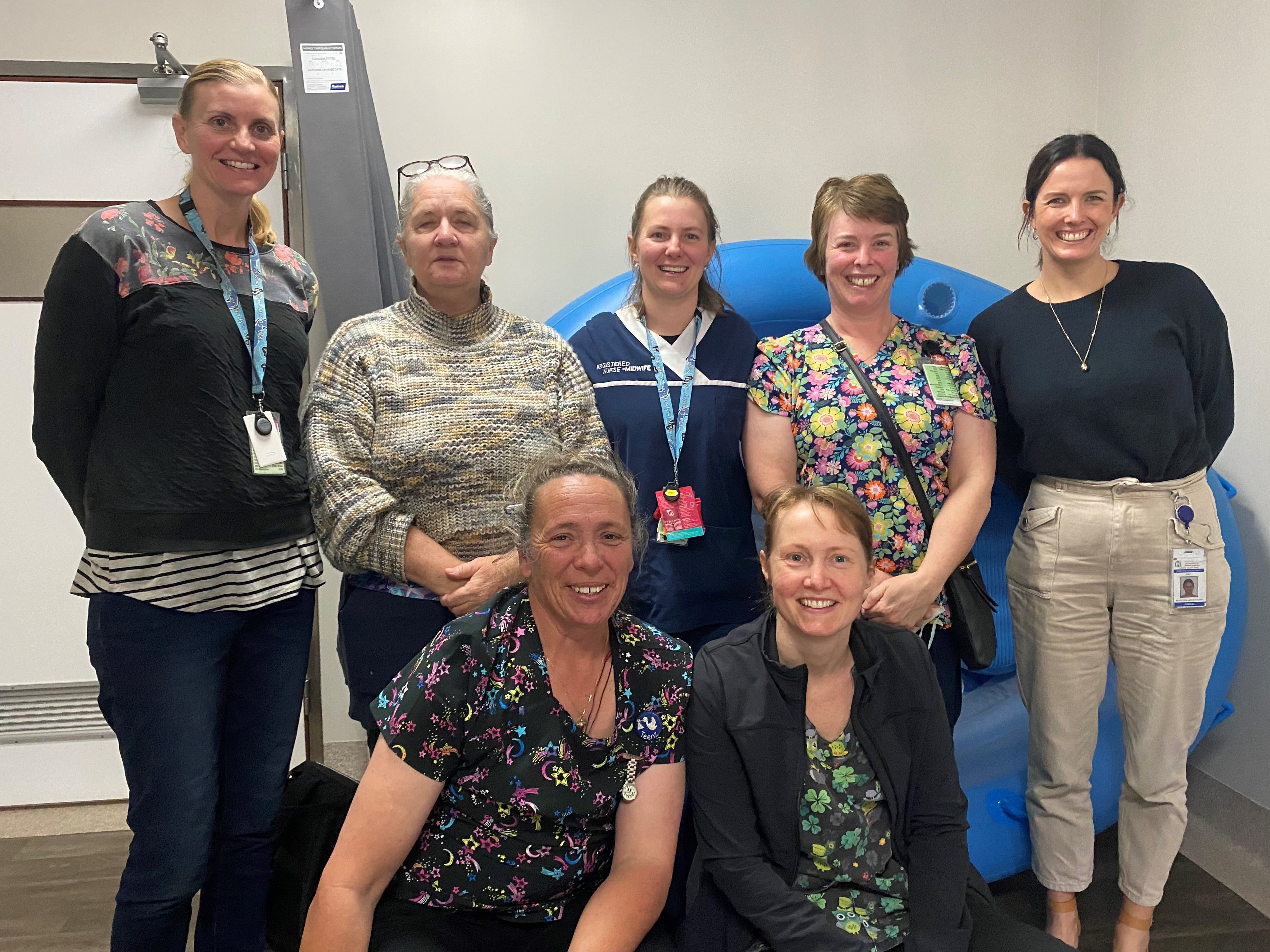 A group of seven nurses stand together smiling