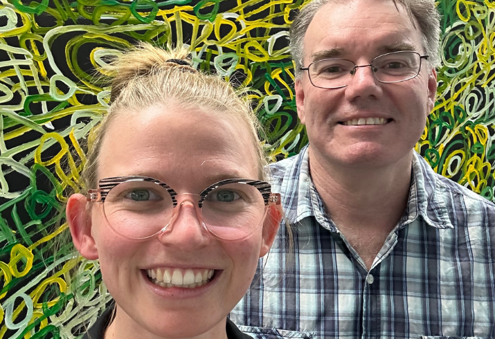 A woman and a man stand in front of an abstract artwork smiling