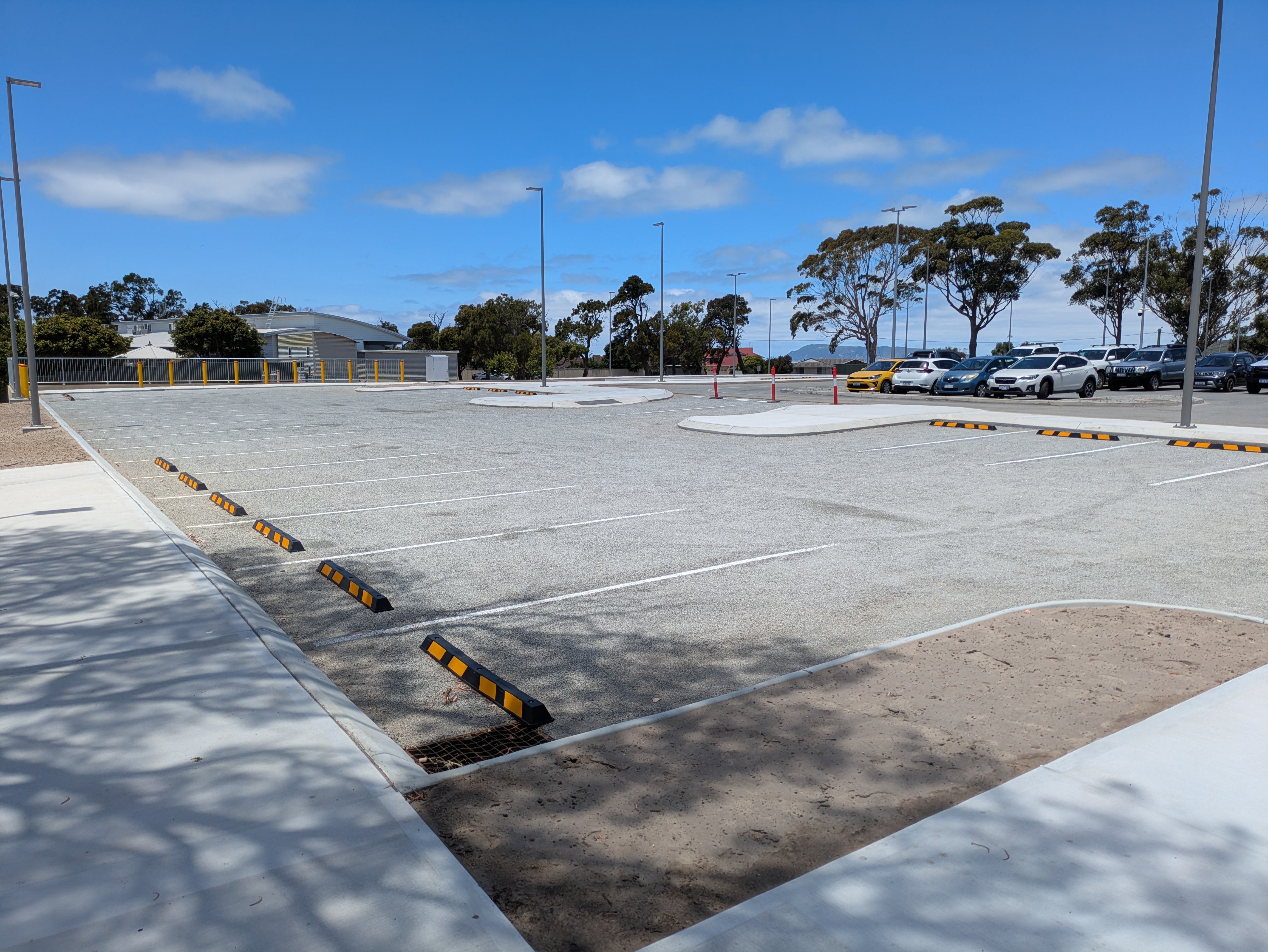 A newly built car park without vehicles, some trees and sky in the background