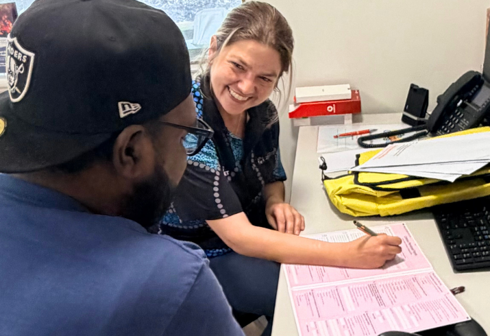 A woman smiles at a man in a black cap as she fills out a pink form