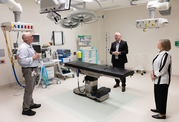 Three people in business attire standing an operating theatre.