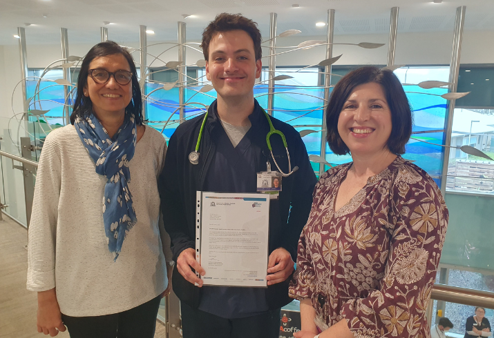 Doctor with stethoscope holding certificate standing in between two women.