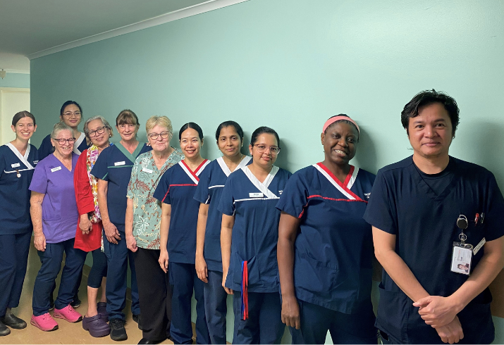 Line of eleven staff in scrubs standing against a green wall.