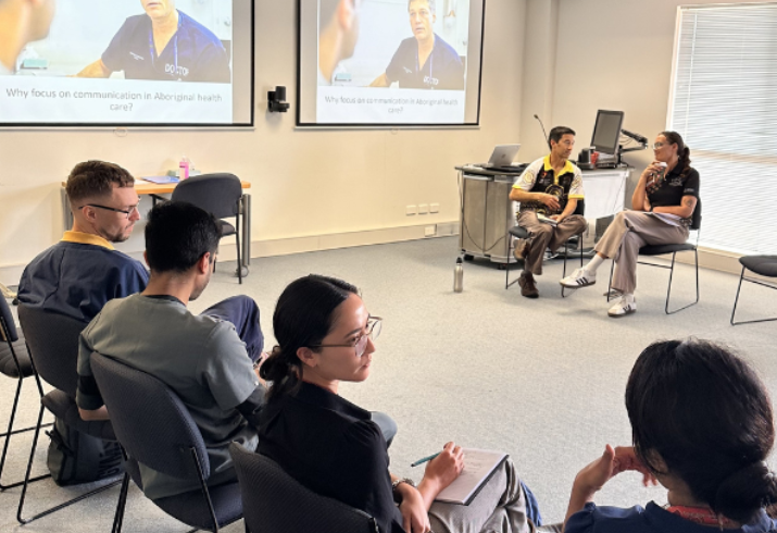 Group of clinicians sitting on chairs in front of presentation screens.