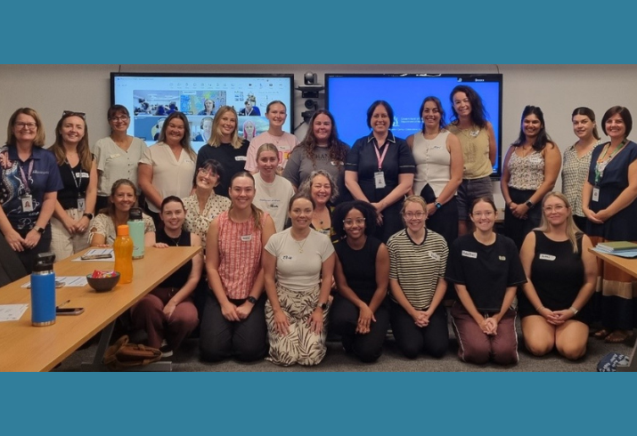 Large group of people standing and kneeling in front of two screens.