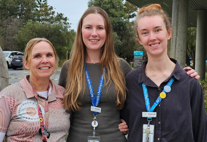 Three women stand outside a building with a car park and modern art visible in the background