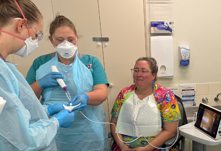 A patient sits in a chair while two speech pathologists prepare for an exploratory procedure
