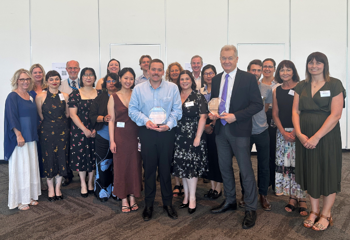 Group standing for photo with two people at the front holding trophies.