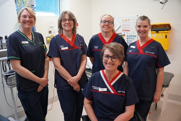 A group of five nurses in a hospital room smiling